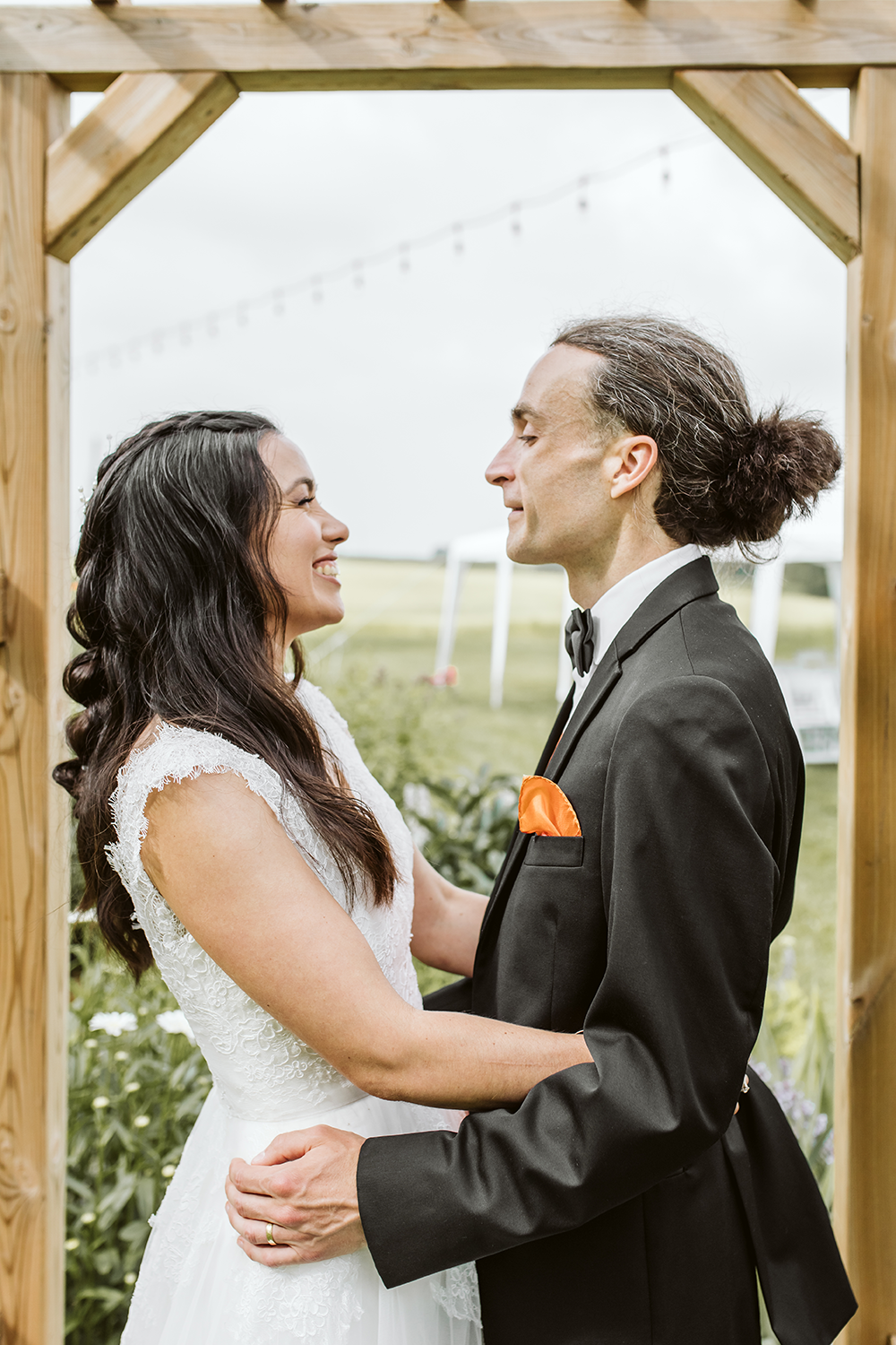 A bride and groom are looking at each other under a wooden archway.