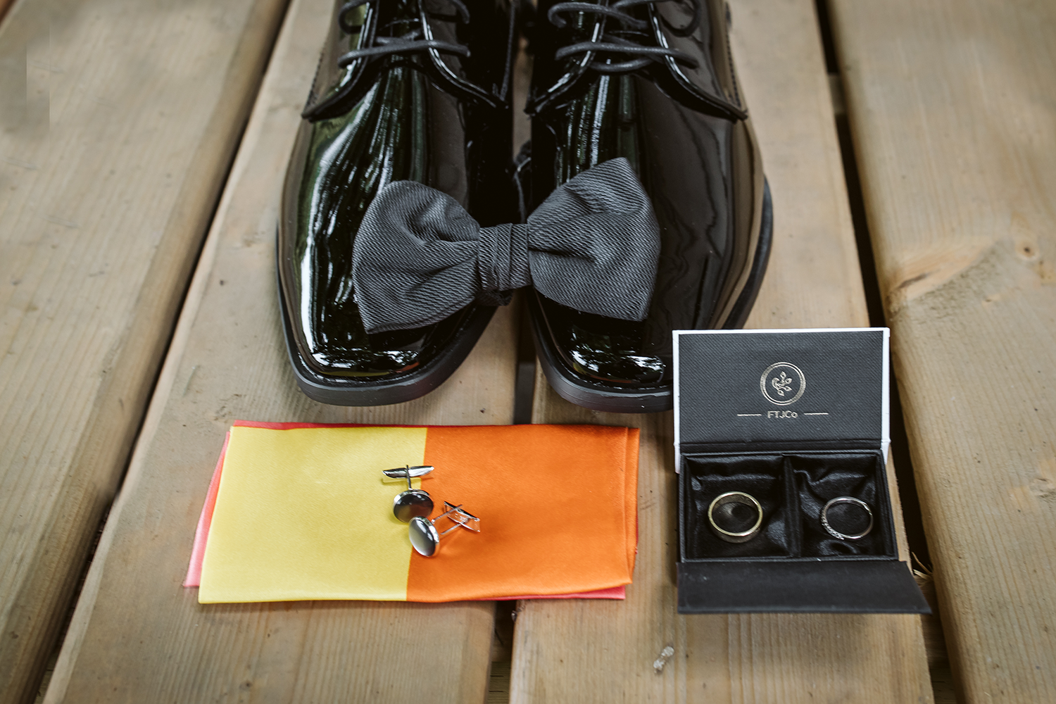 A pair of black shoes with a bow tie and cufflinks on a wooden table.