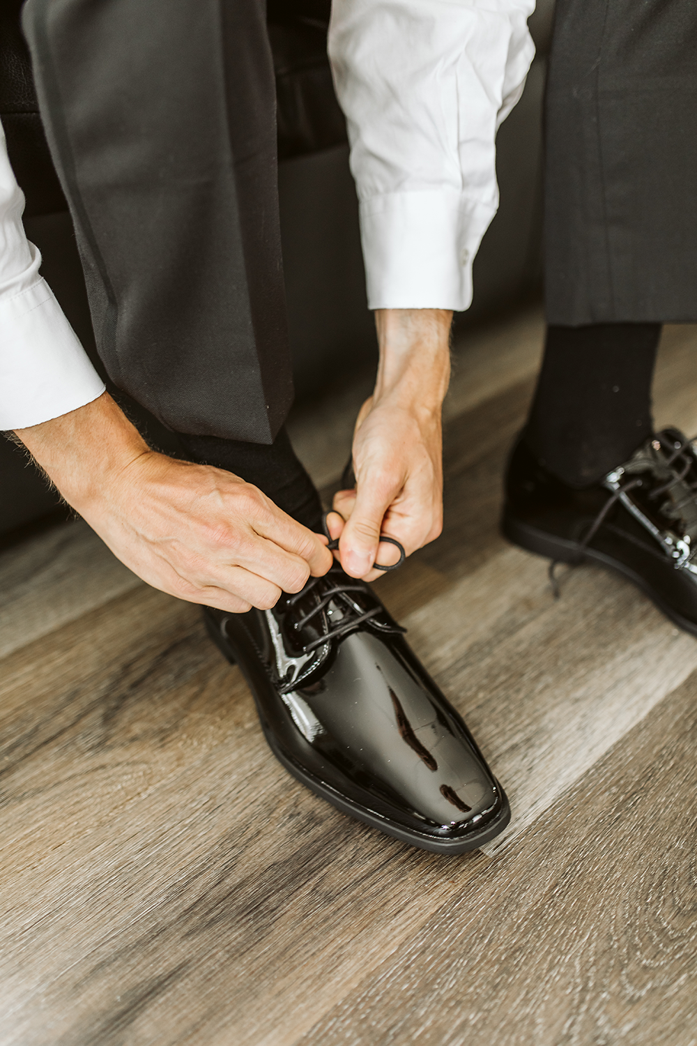 A man is tying his shoes on a wooden floor.