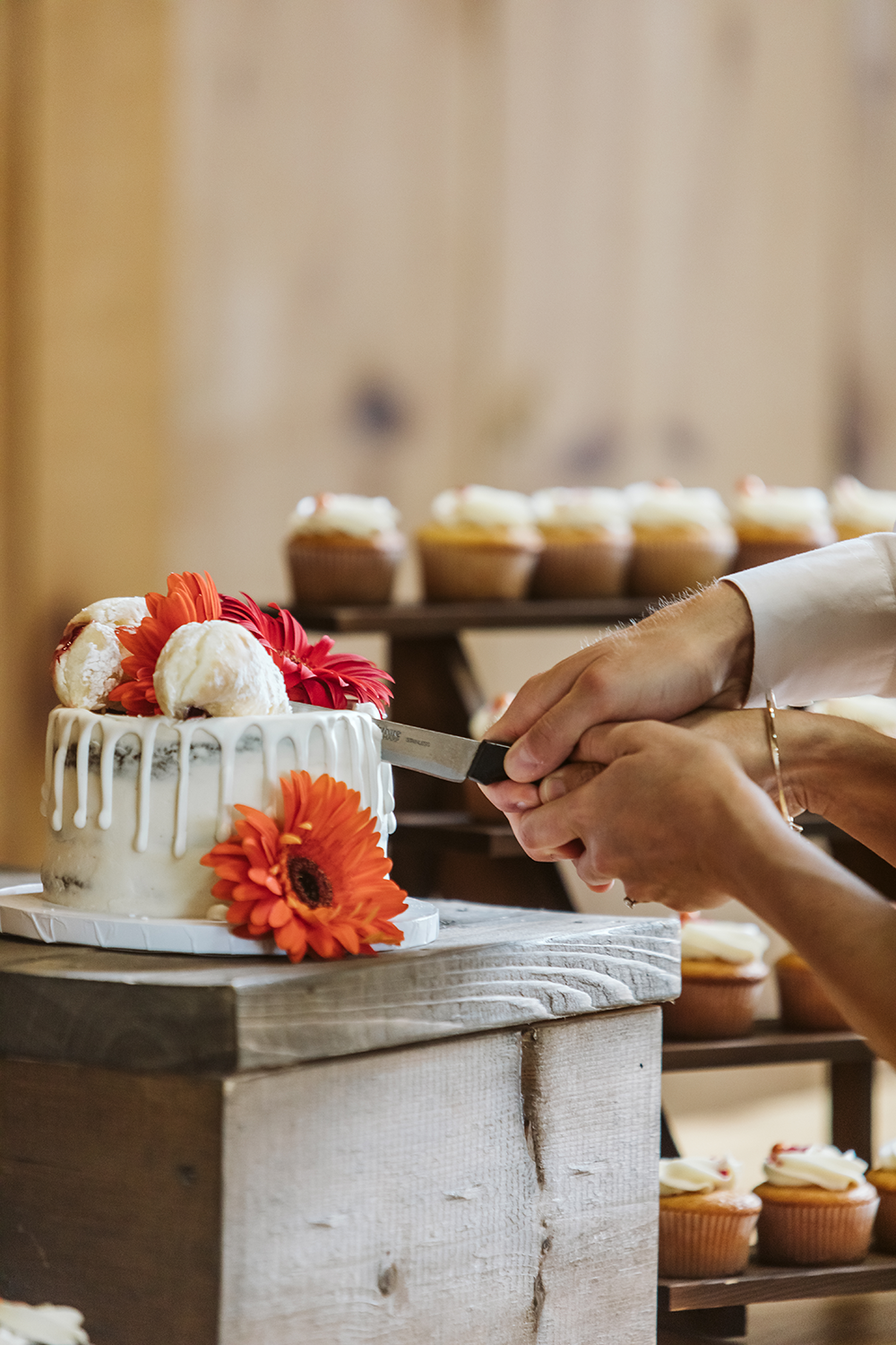 A bride and groom are cutting their wedding cake with cupcakes in the background.