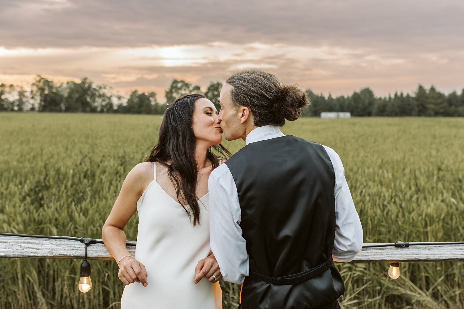 A bride and groom are kissing in a field of wheat.