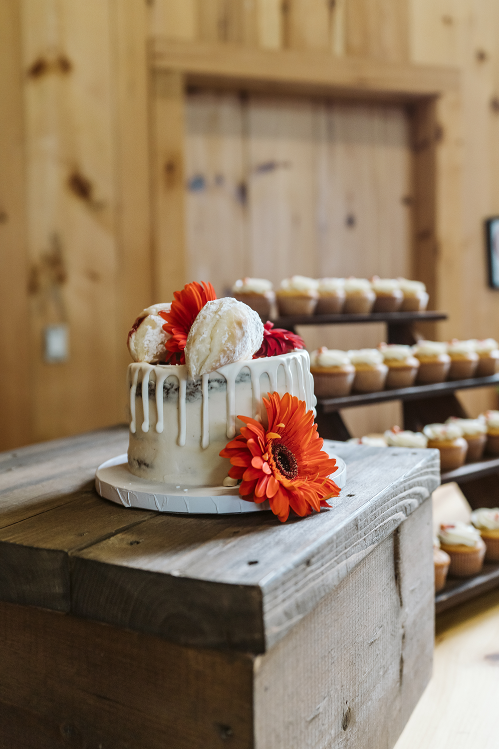 A wedding cake is sitting on top of a wooden table next to cupcakes.
