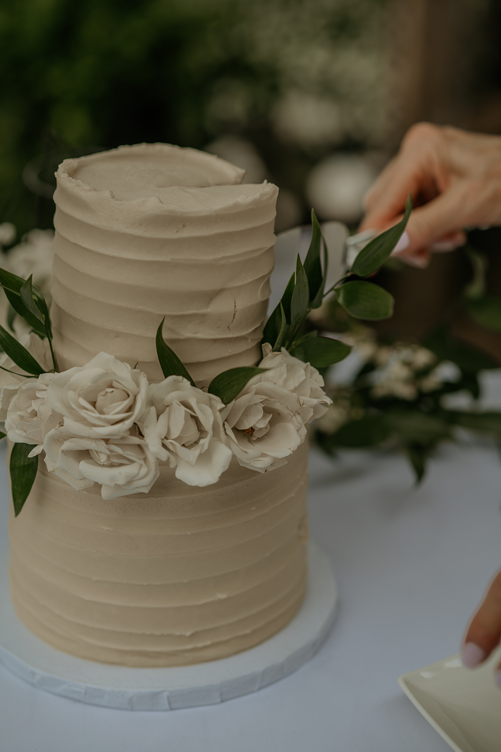 A person is cutting a wedding cake with flowers on it.