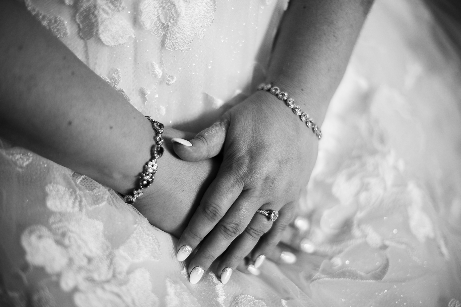 A black and white photo of a bride wearing a bracelet and a wedding ring.