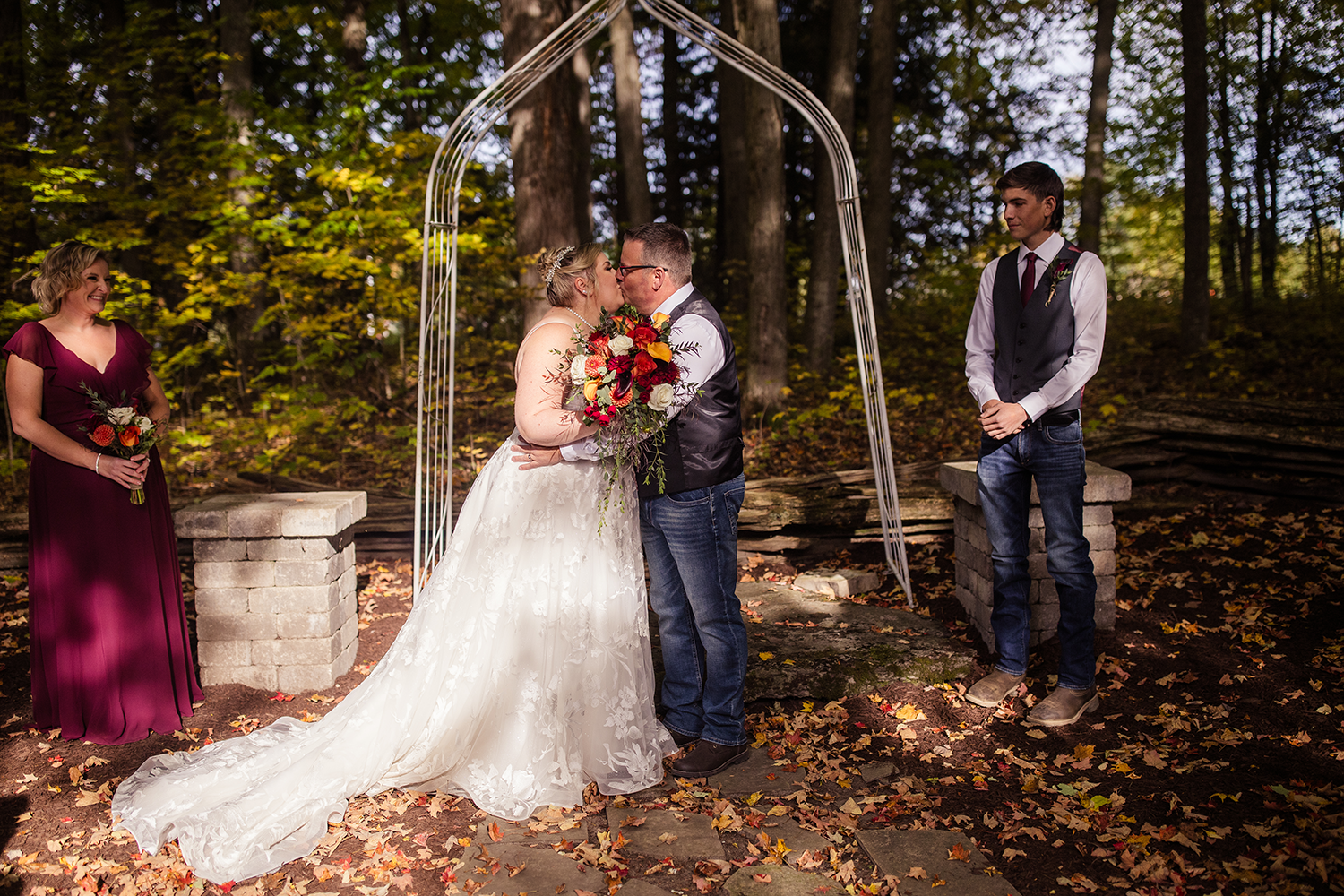 A bride and groom kissing during their wedding ceremony in the woods.