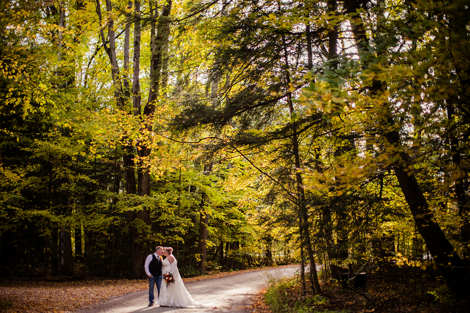 A bride and groom are walking down a dirt road in the woods.