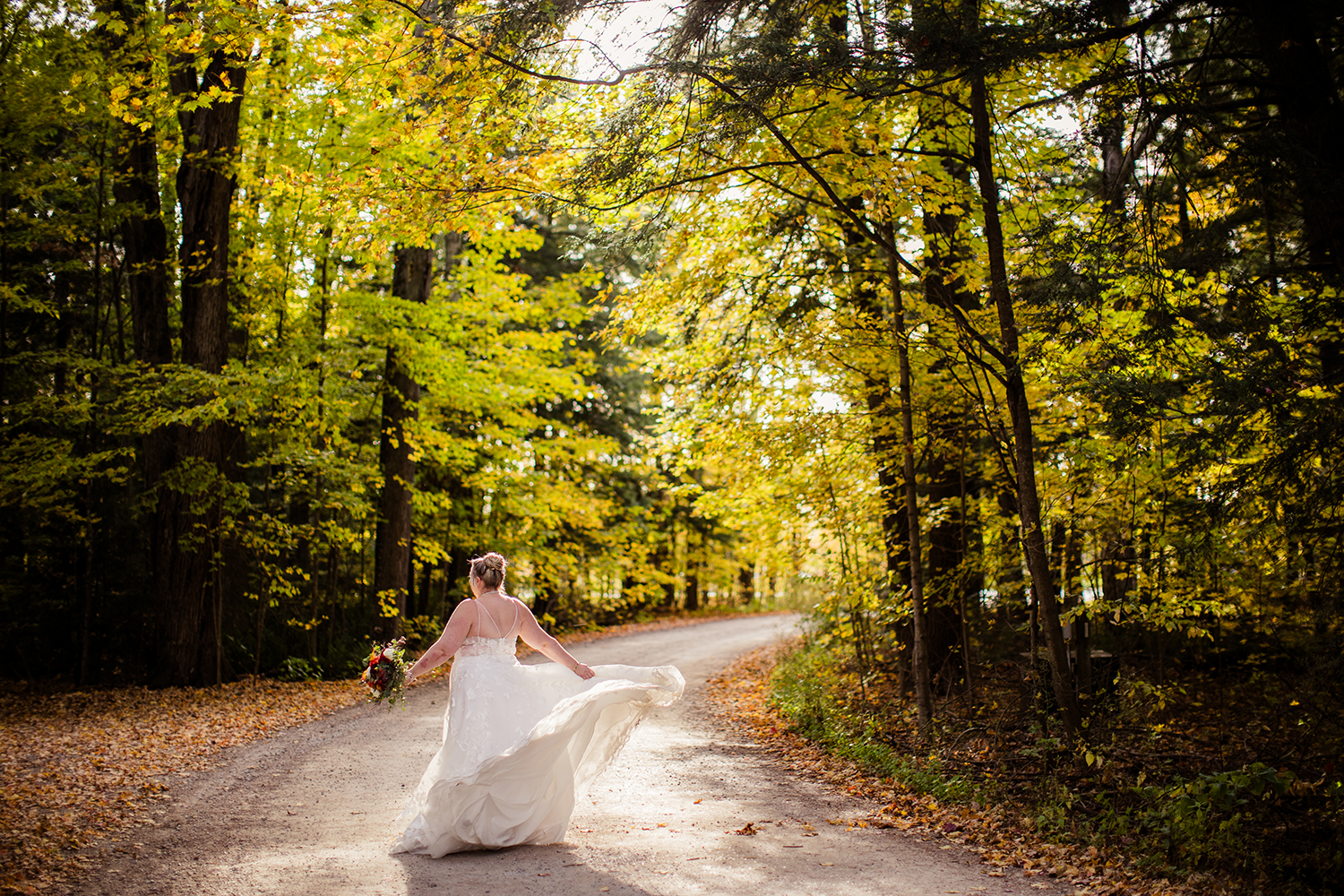 A bride in a wedding dress is walking down a dirt road in the woods.