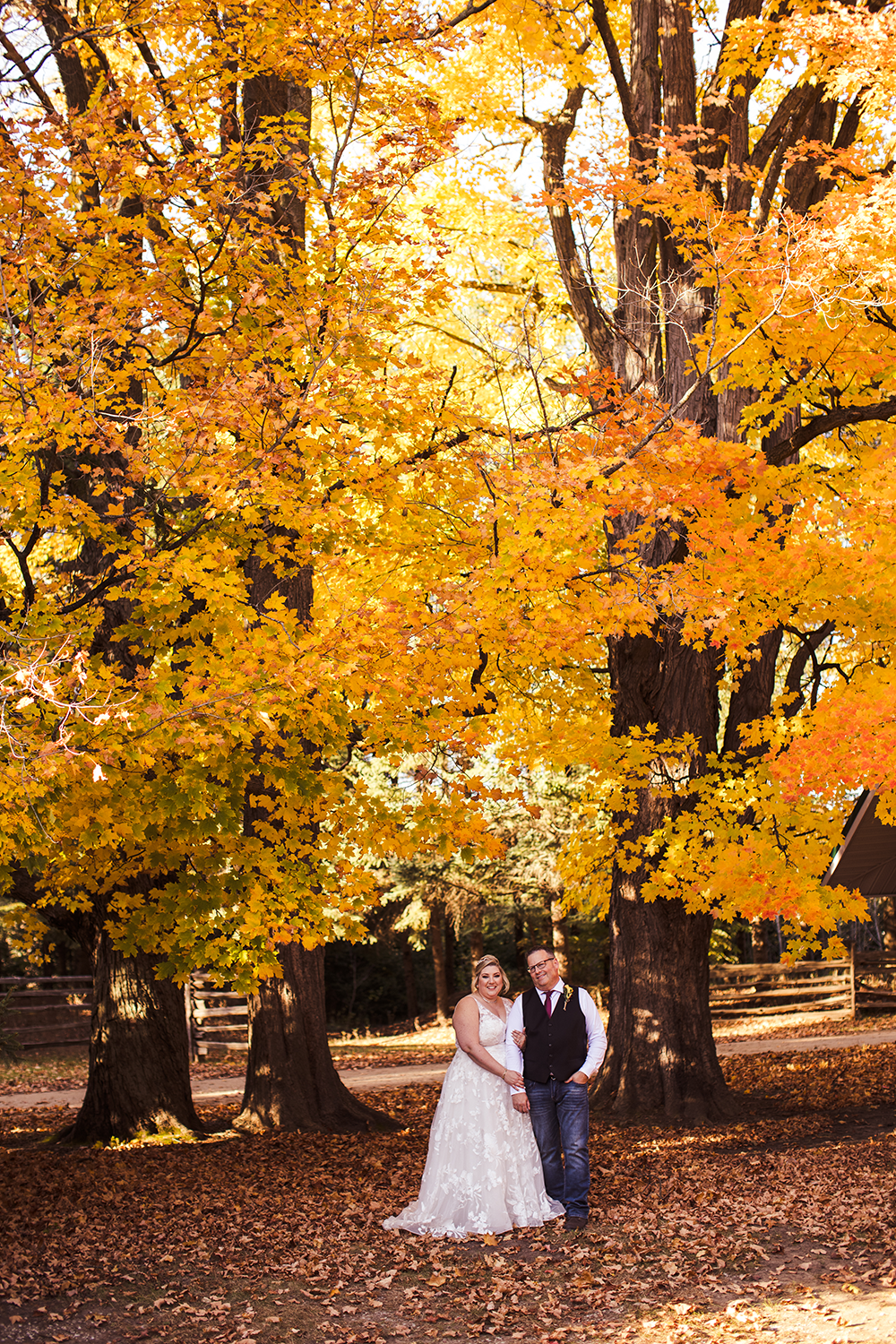 A bride and groom are posing for a picture in front of trees with yellow leaves.