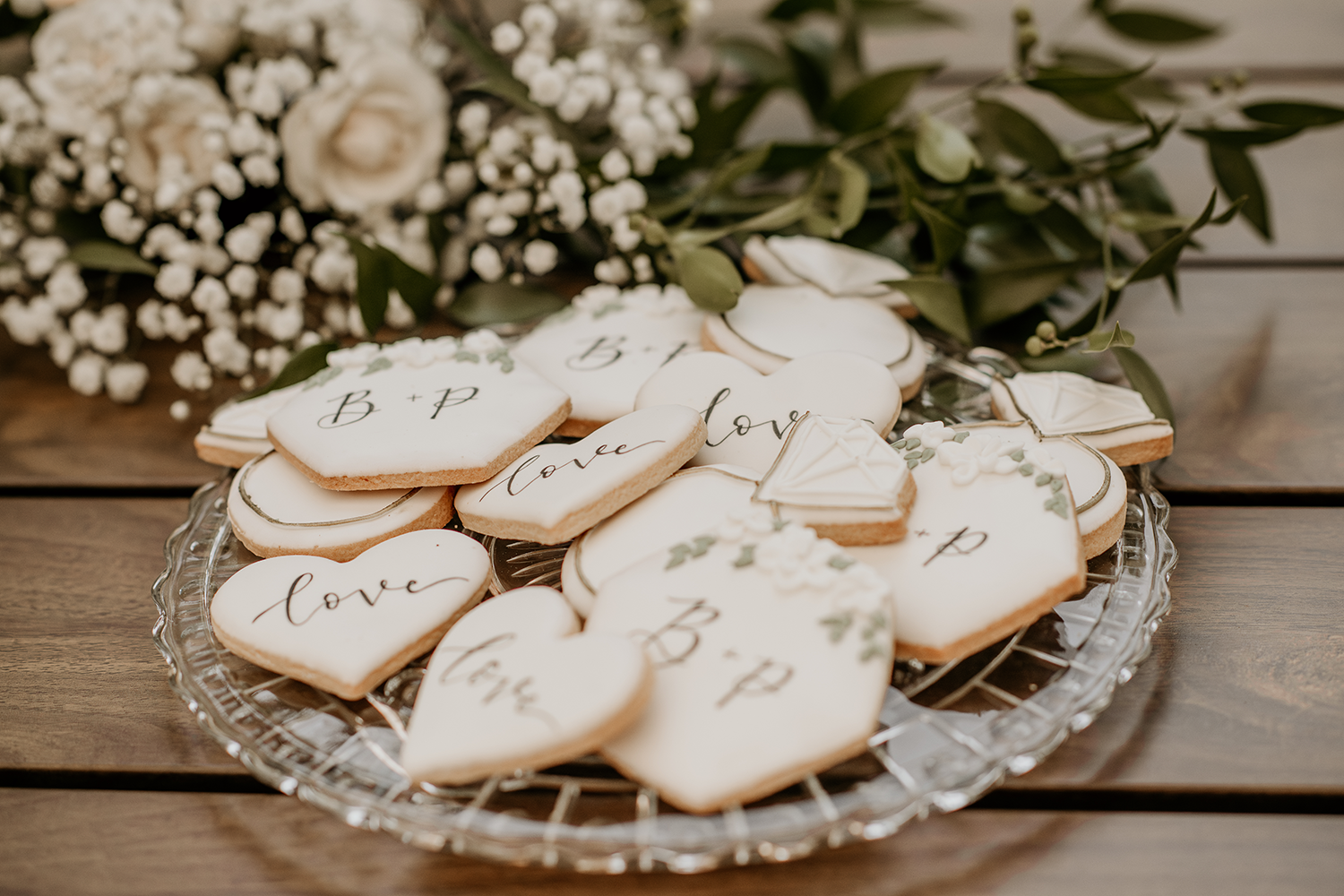 A glass plate topped with heart shaped cookies next to a bouquet of flowers.