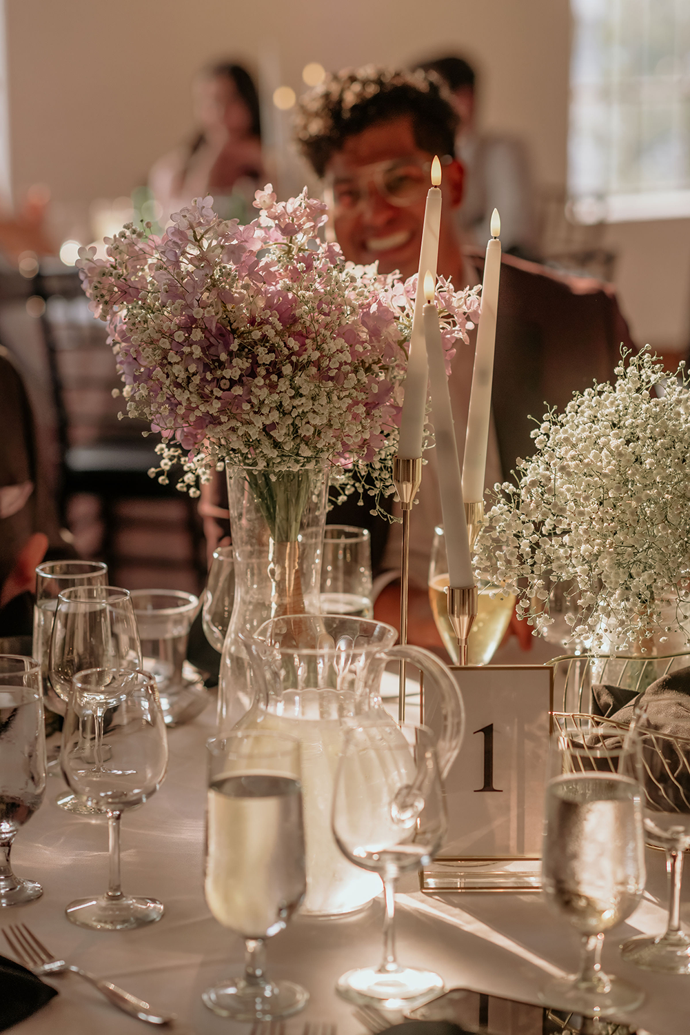 A man is sitting at a table with a vase of baby 's breath and candles.