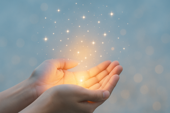 Hands cupped, glowing with golden light and sparkling stars, set against a blurred blue background.