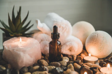 A bottle of essential oil is sitting on top of a pile of rocks next to candles.
