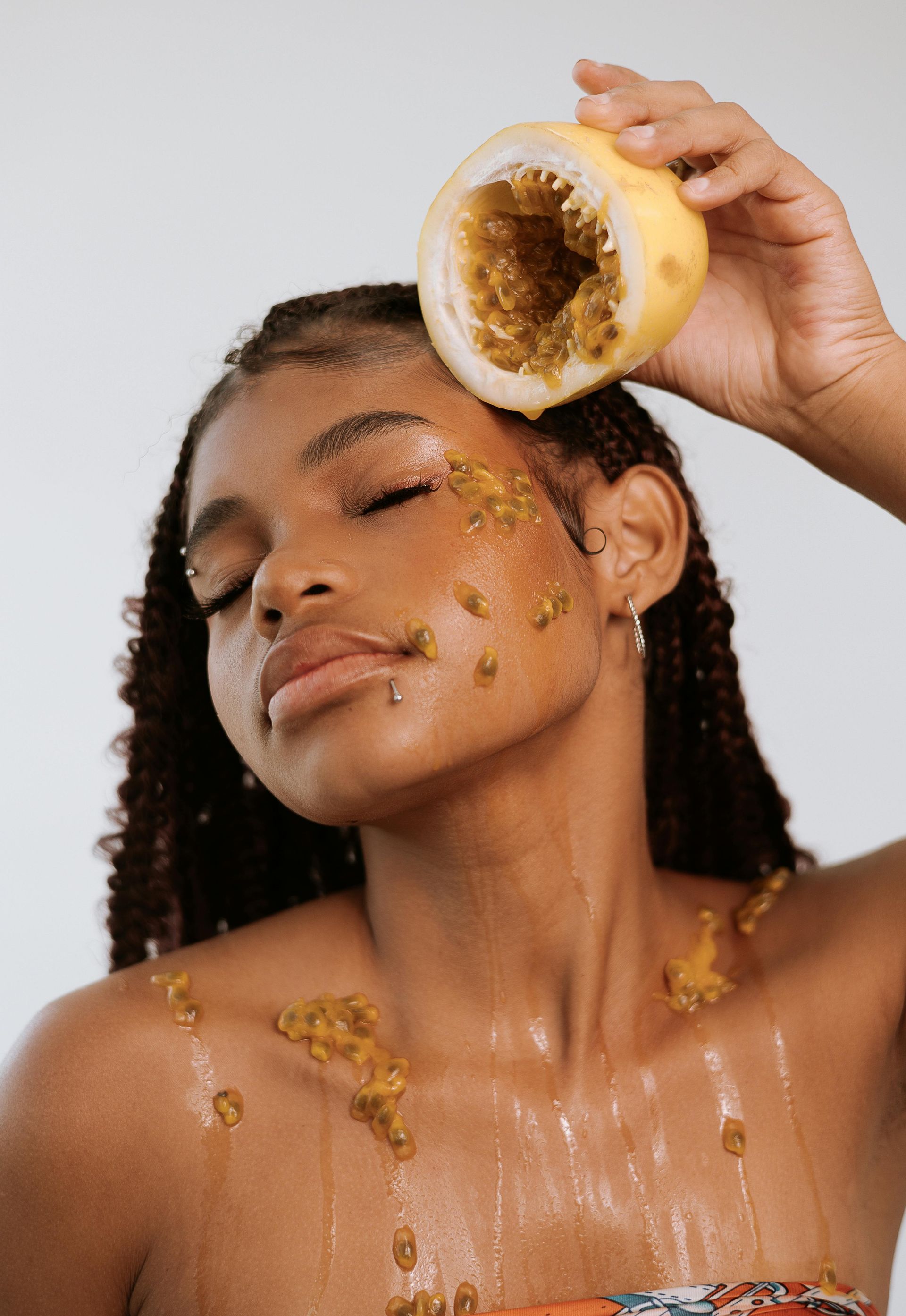A woman is holding a slice of passion fruit on her face.