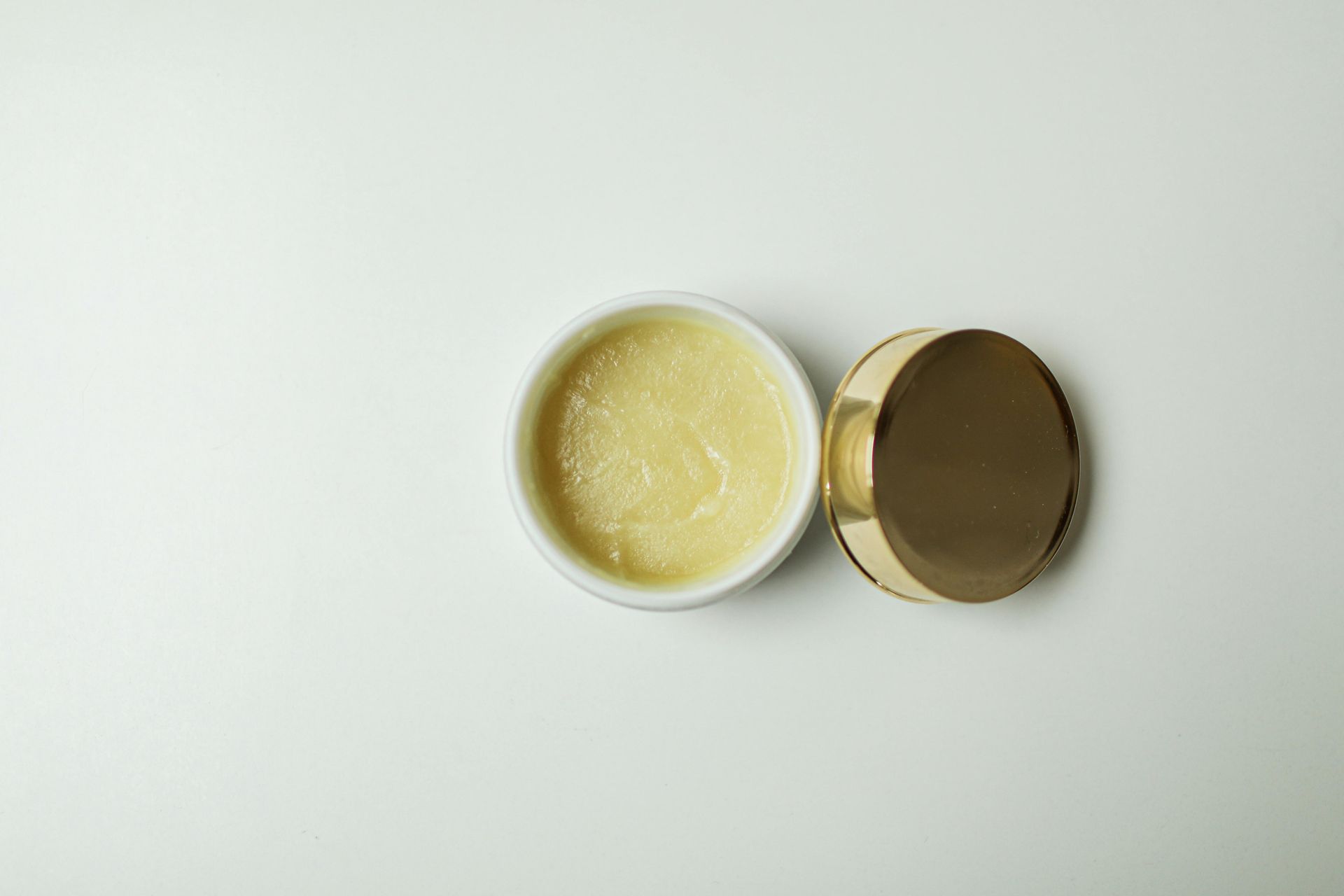 A small bowl of cream with a gold lid on a white surface.