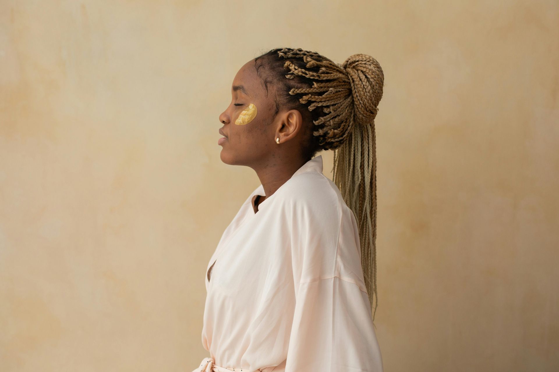 A woman with braids is wearing a robe and a gold mask on her face.