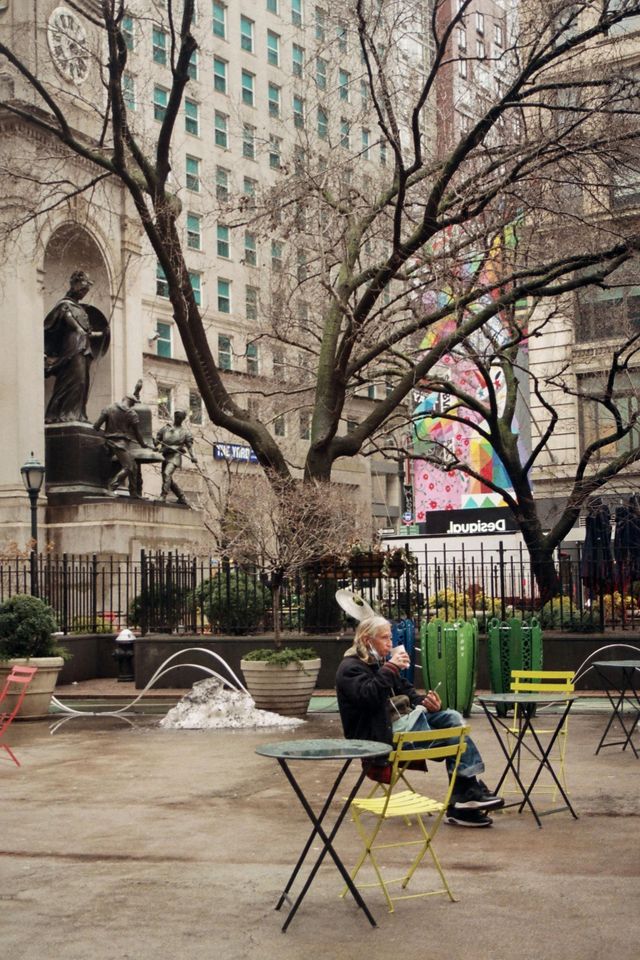 A man sits at a table in a park with a statue in the background