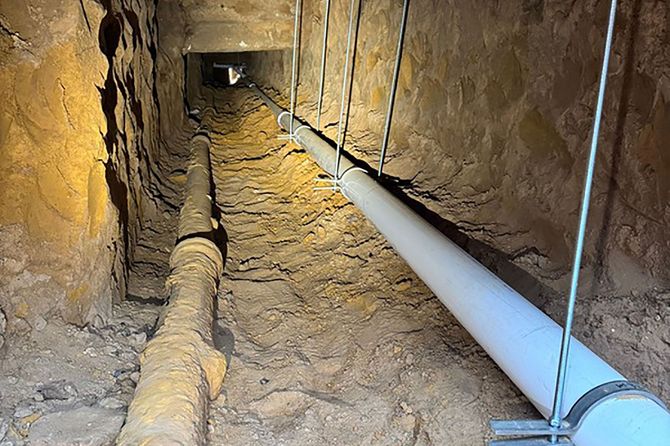 Copper and black pipes against a gray concrete wall, part of a building’s plumbing system.