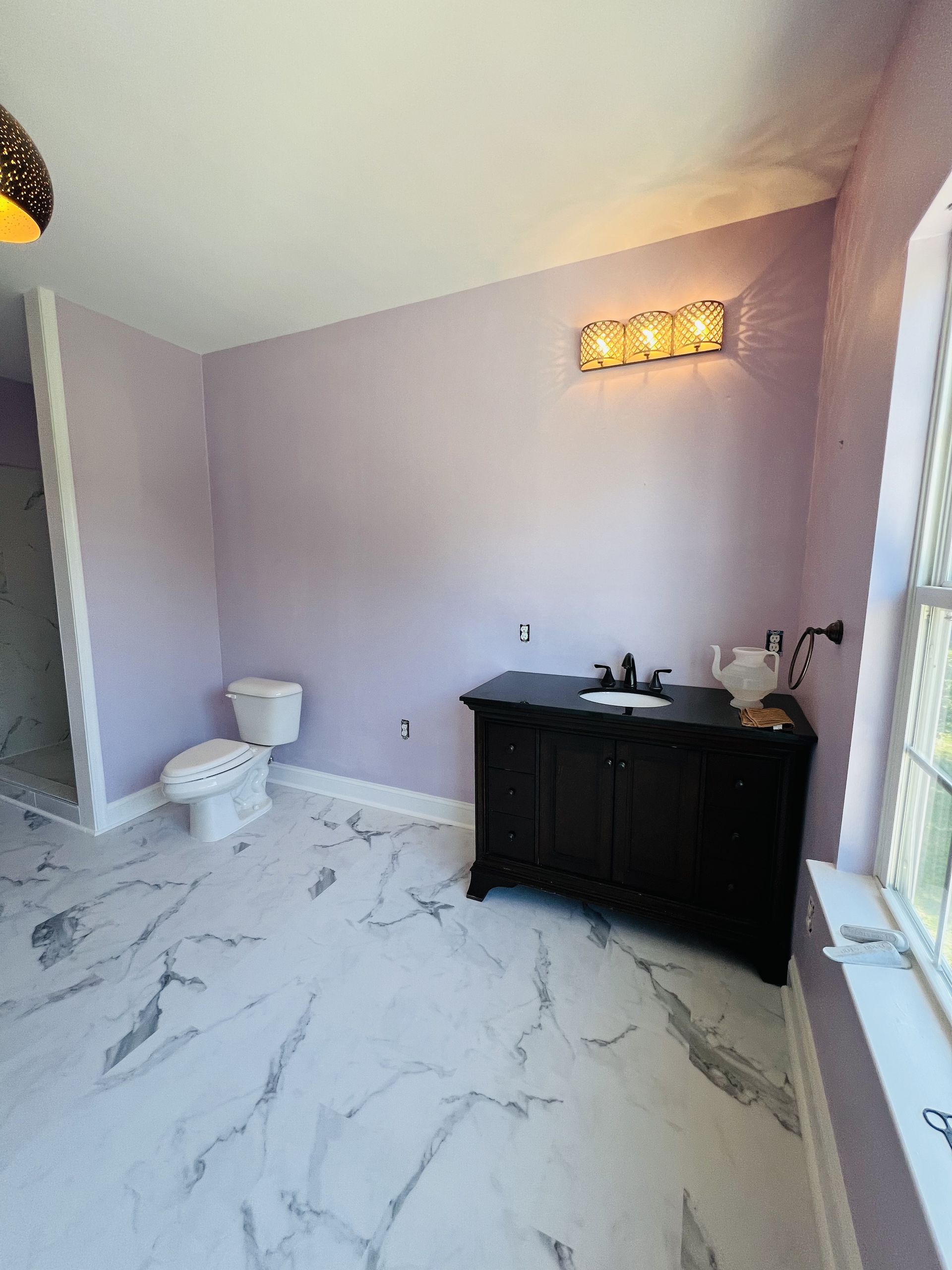 A bathroom with purple walls , a toilet , a sink , and a window.