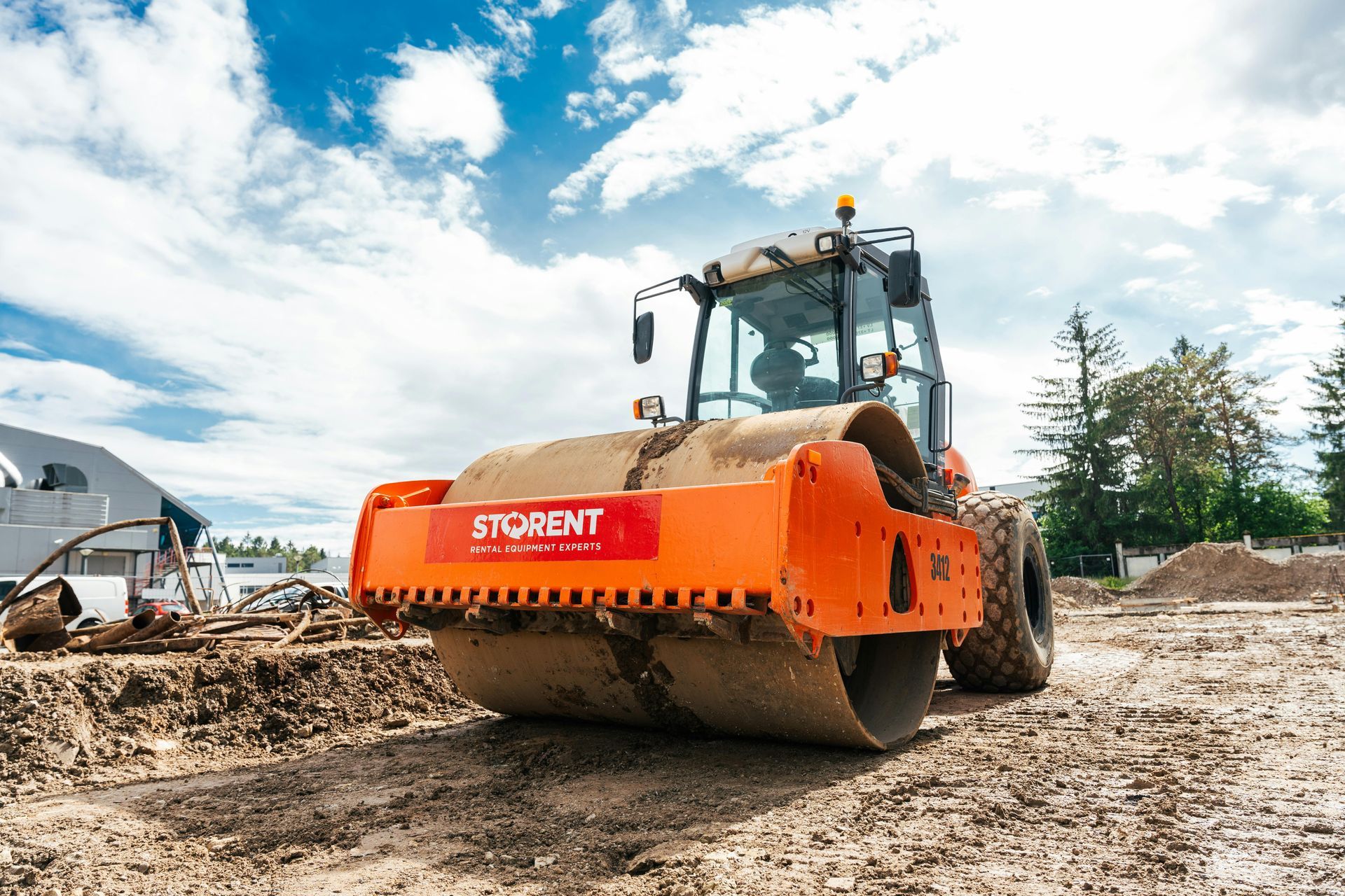 A large orange roller is sitting on top of a dirt field.