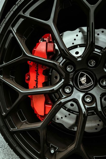 Close-up of a black Lamborghini wheel with red brake calipers and the Lamborghini logo.