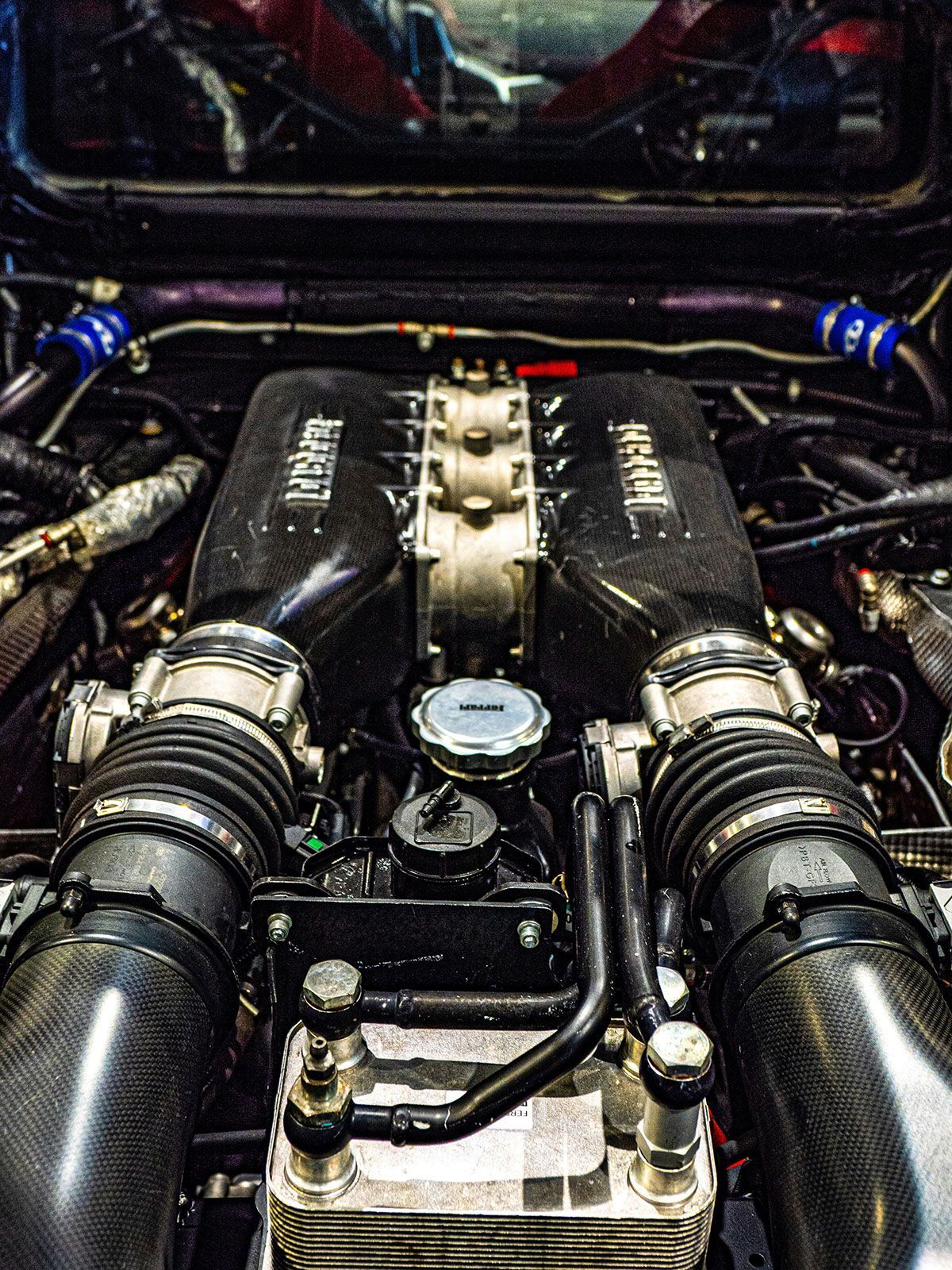 Close-up of a high-performance car engine, with carbon fiber components, intakes, and blue hoses.