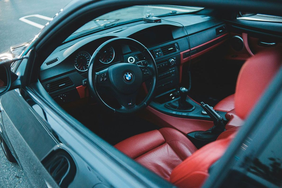 Black BMW interior with red leather seats, dashboard, and trim; steering wheel in focus.
