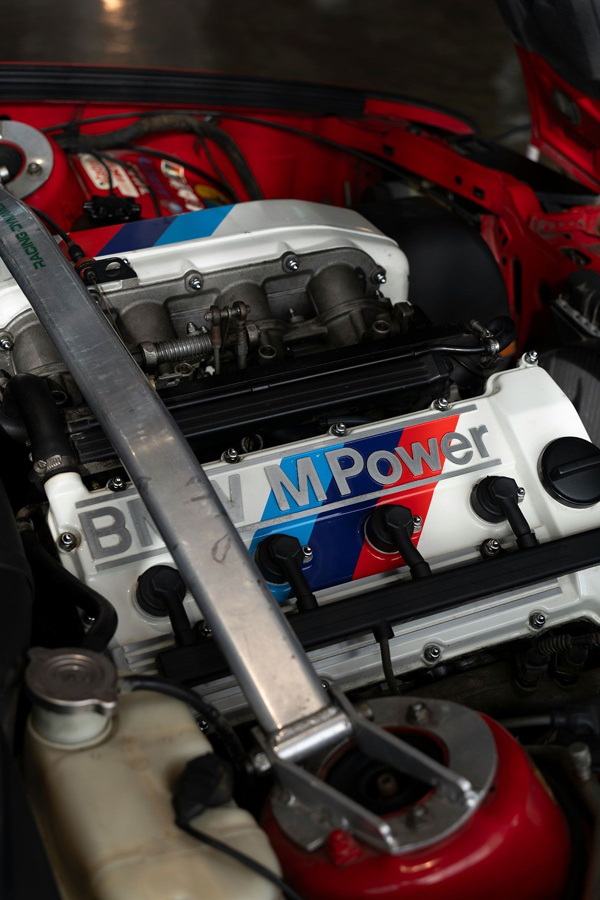 BMW M Power engine with strut bar in a car engine bay. Red, white, and blue colors prominent.