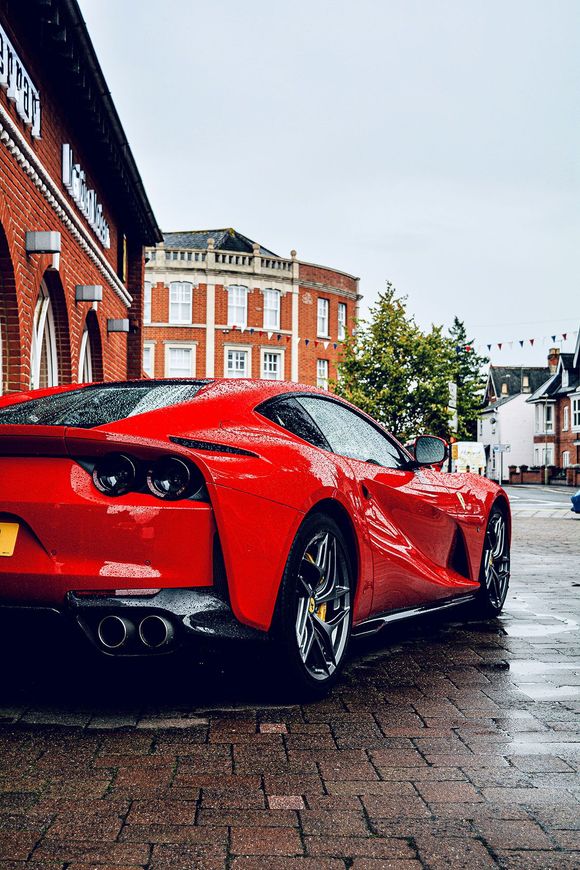 Red Ferrari parked on wet brick street near a building with multiple windows.