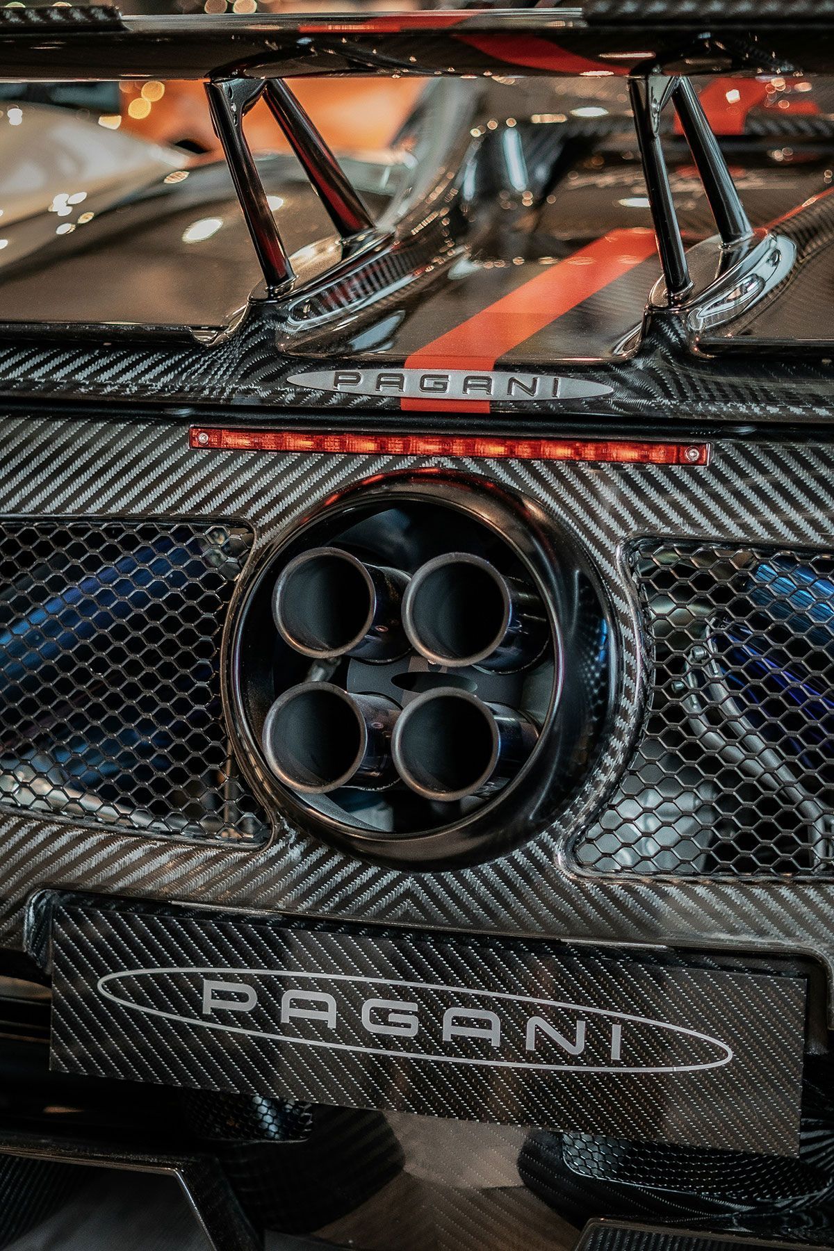 Close-up of Pagani car exhaust with four circular pipes, carbon fiber details, and Pagani logo.