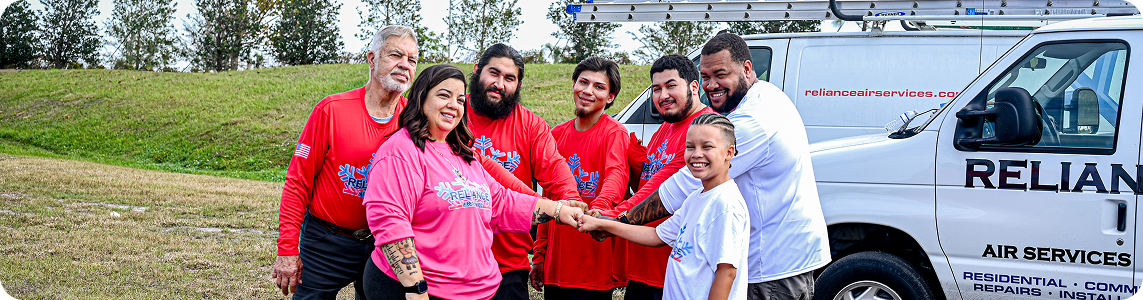 Group of people in red and pink shirts, and a child in white, with hands together near a white van.