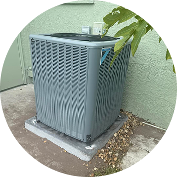 Gray air conditioning unit outside a light green stucco wall.