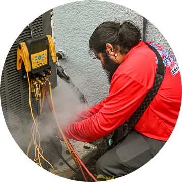 HVAC technician in red shirt working on AC unit, steam present, with diagnostic tools attached.