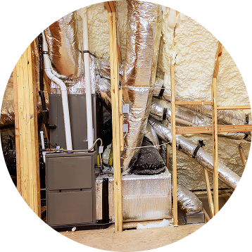 HVAC system installation in a wooden framed space. Silver ducts, gray unit, spray foam insulation.