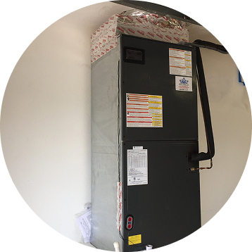 An air conditioning unit is in a corner of a room, with ductwork on top.