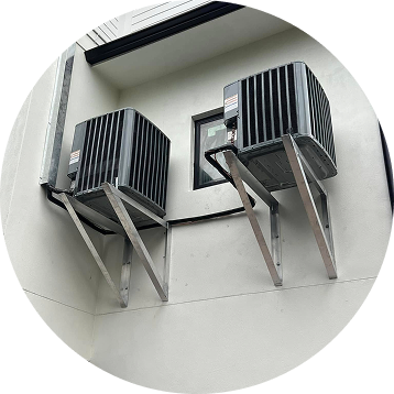Two black air conditioning units mounted on silver brackets on a white exterior wall.