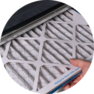 Hand holding a new air filter, ready to replace an old one in an HVAC system.