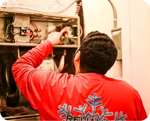Person in red shirt works on furnace, indoors.