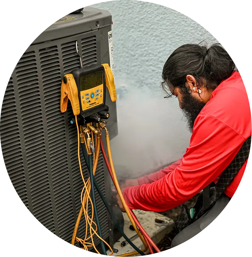 HVAC technician working on an air conditioning unit outside, connecting gauges, with visible mist.