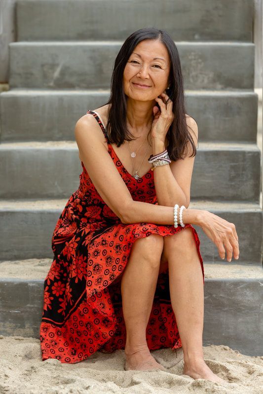 Woman with dark hair in red patterned dress sits on outdoor stairs, smiling.