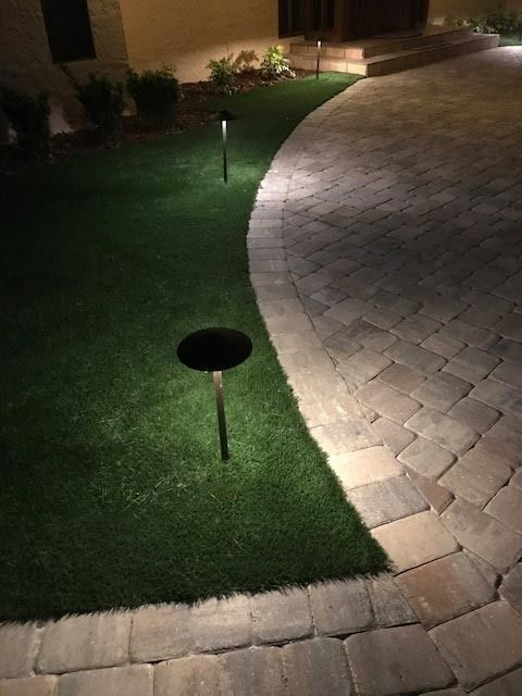 Pathway illuminated by small lights, curving next to green lawn at night.