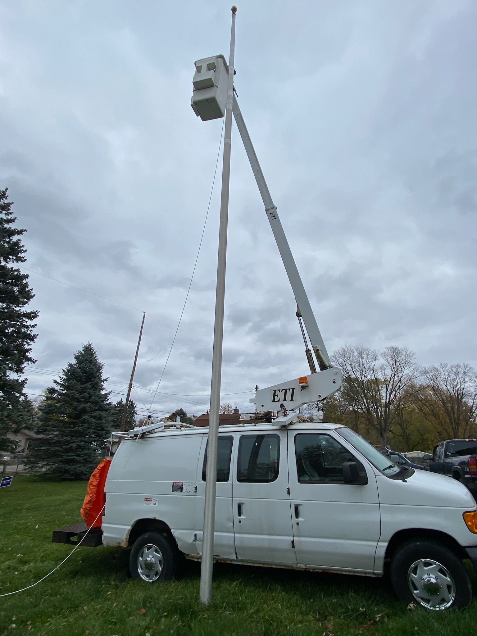 A white van with a crane on top of it is parked in a grassy field.