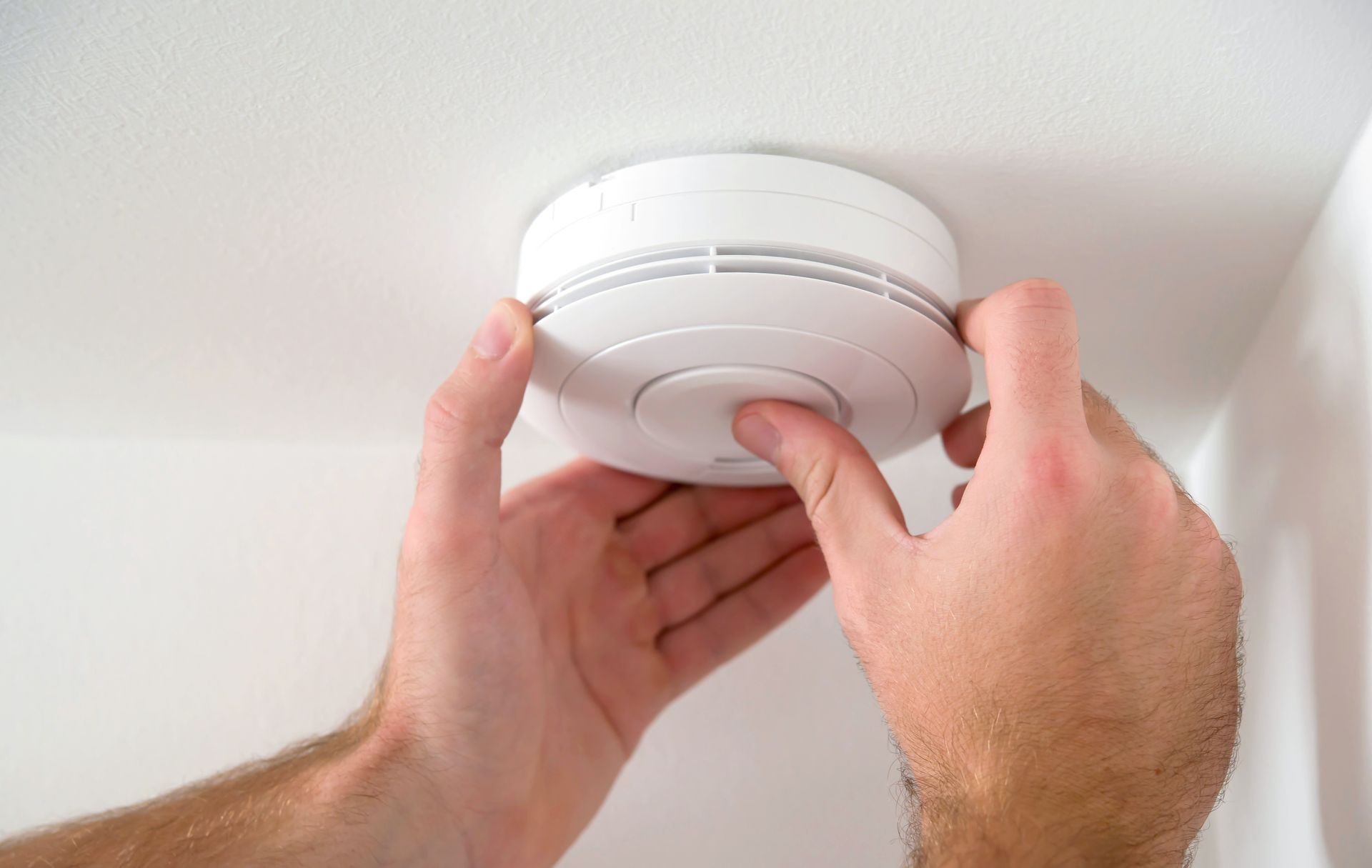 A person is installing a smoke detector on the ceiling.