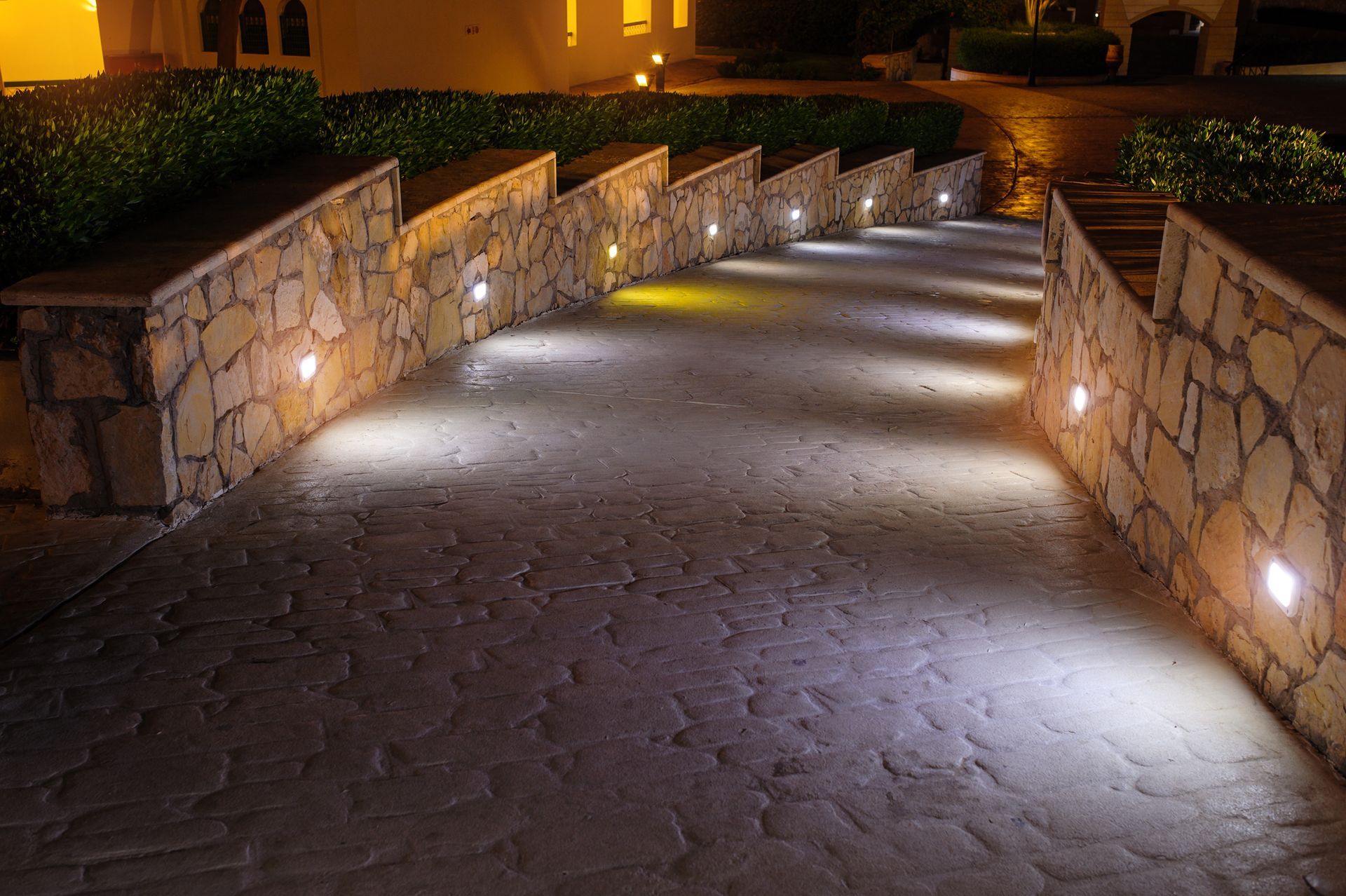 A stone walkway with lights on the side of it at night.