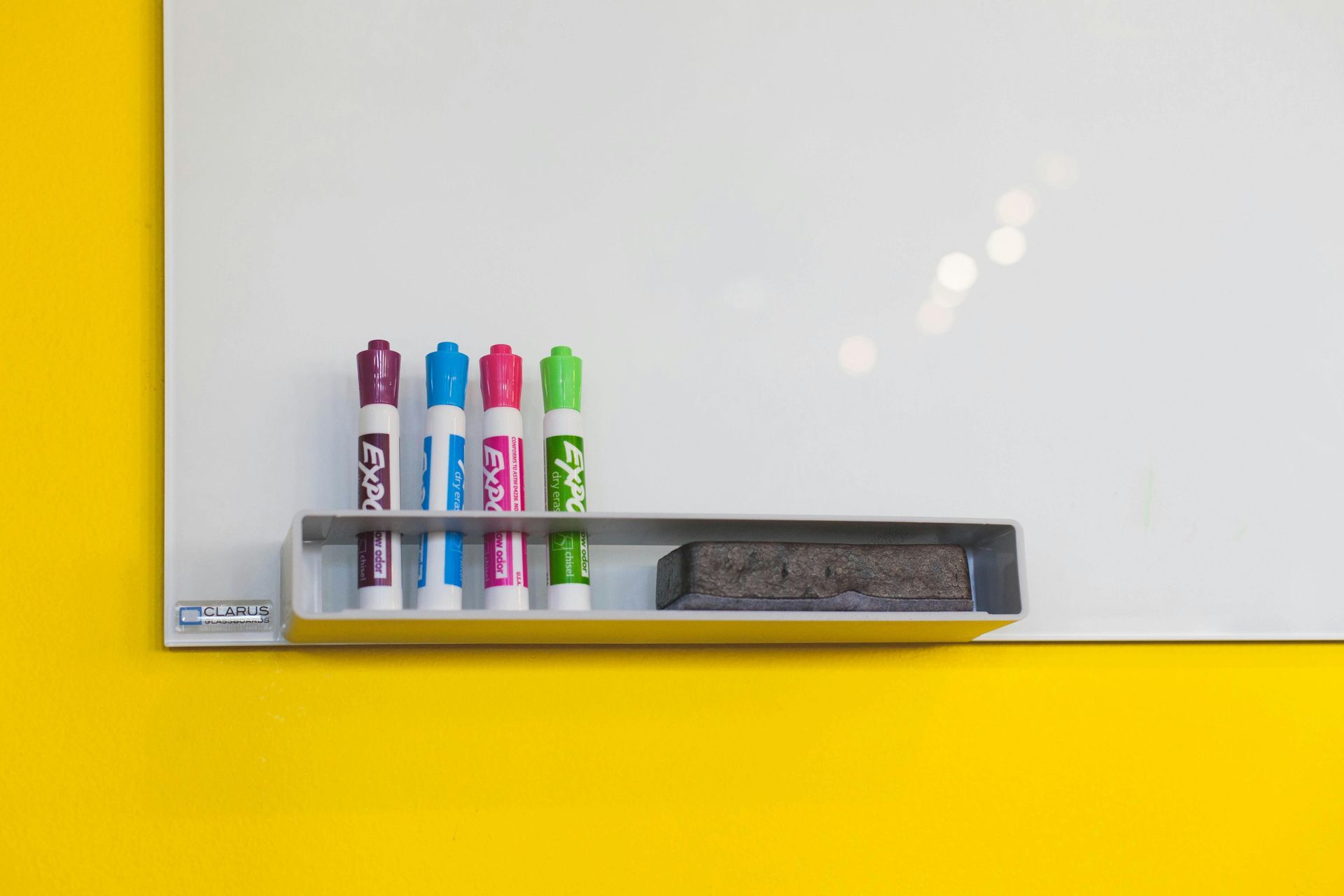 Whiteboard with markers and eraser on yellow wall.