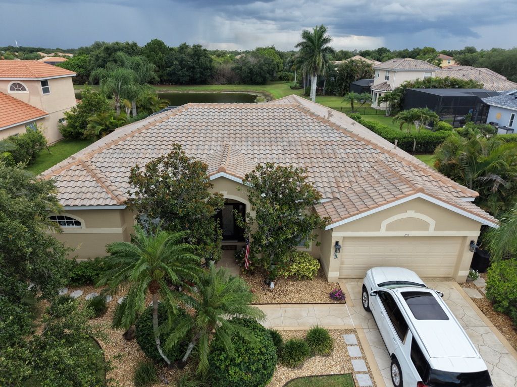 Aerial view of a beige house with a tiled roof, front palm trees, and a white SUV in the driveway.