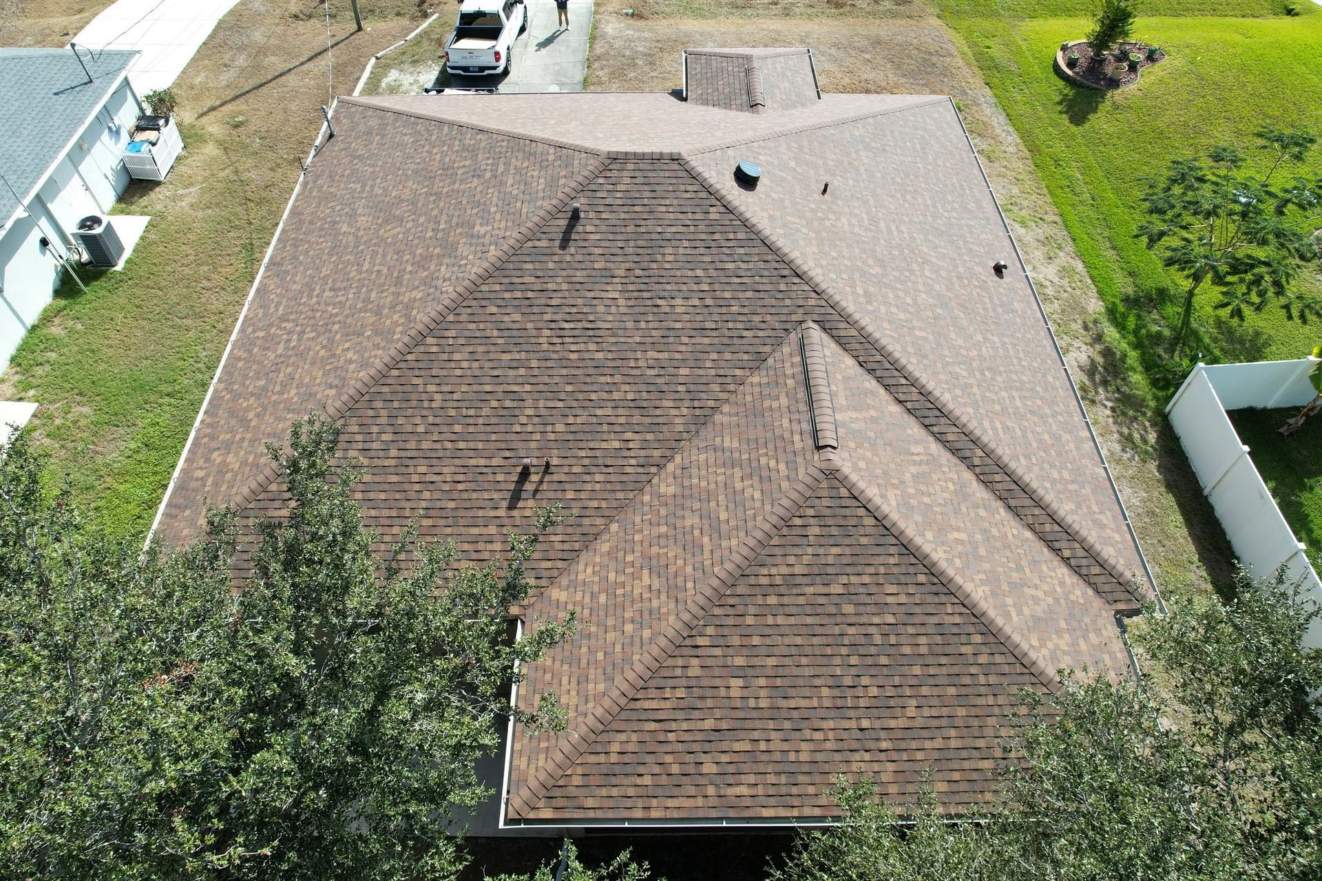Aerial view of a brown shingled house roof with trees and a driveway nearby