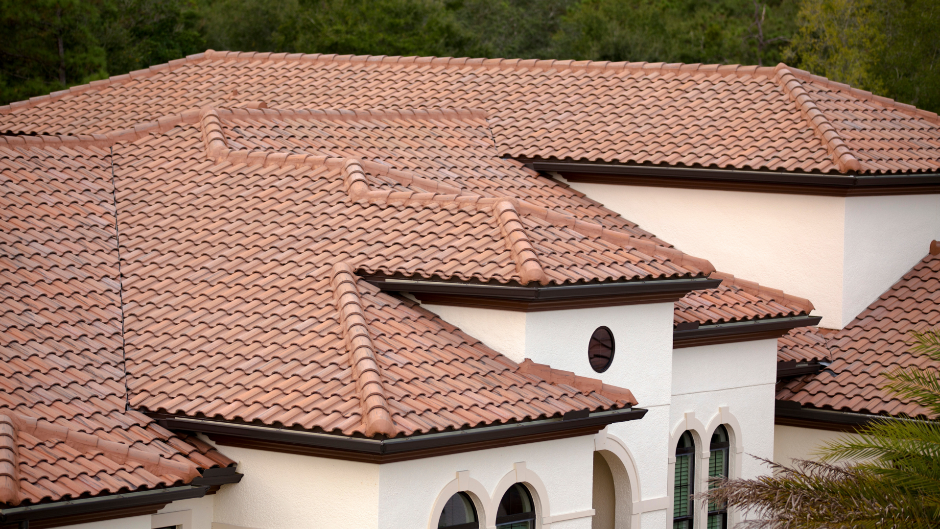Tiled terracotta roof over a white stucco building with arched windows and a small circular opening