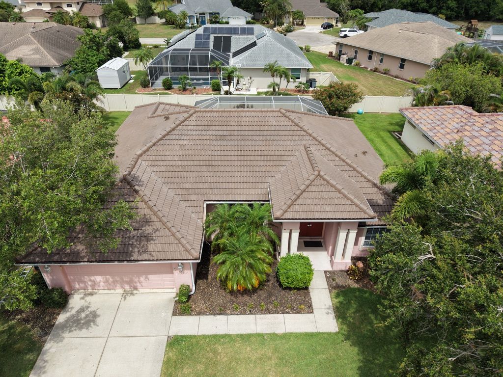 Aerial view of a suburban house with a brown roof, driveway, and front yard greenery