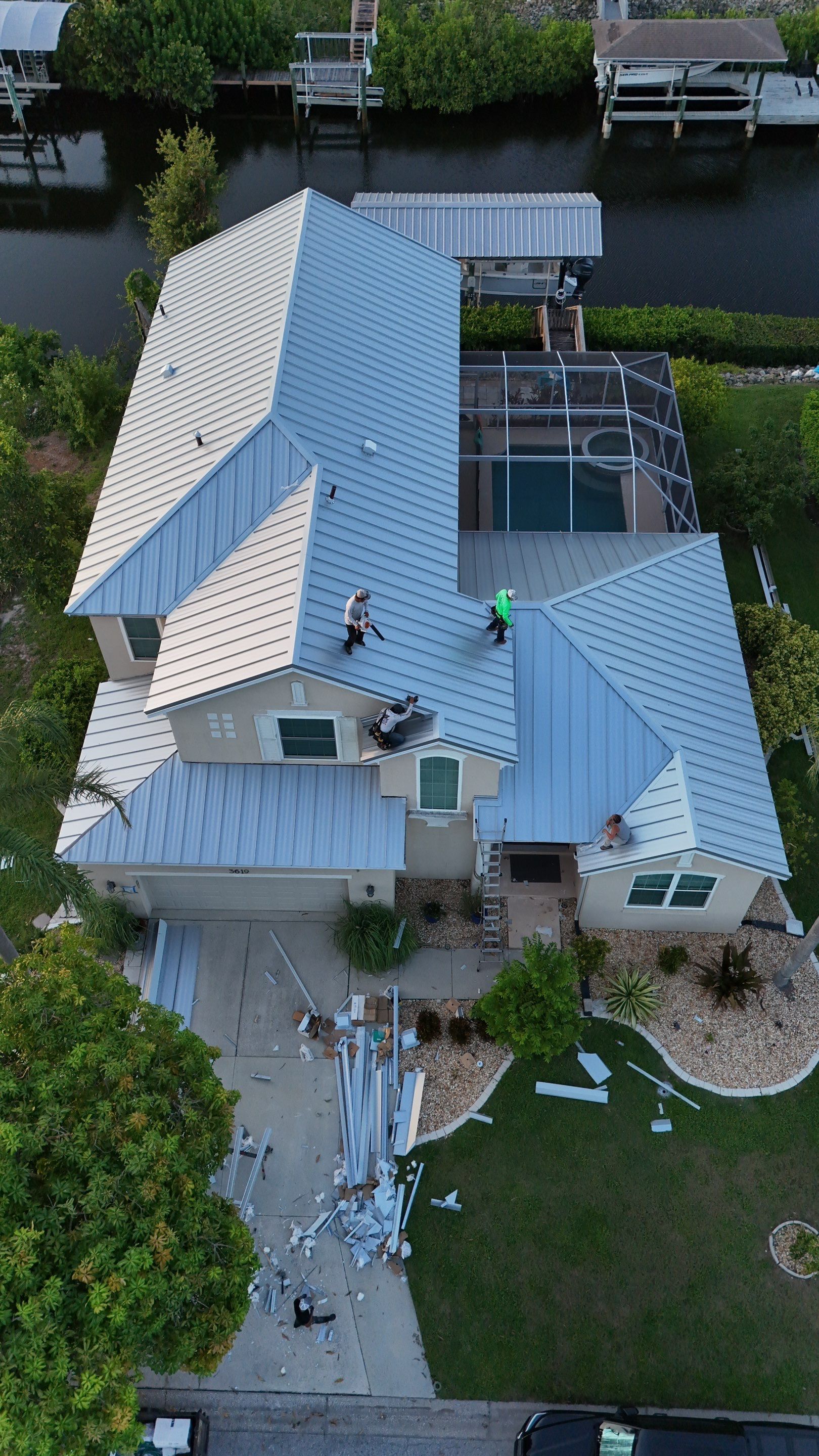 Aerial view of a light-blue house with a boat dock on a canal, surrounded by trees and a driveway