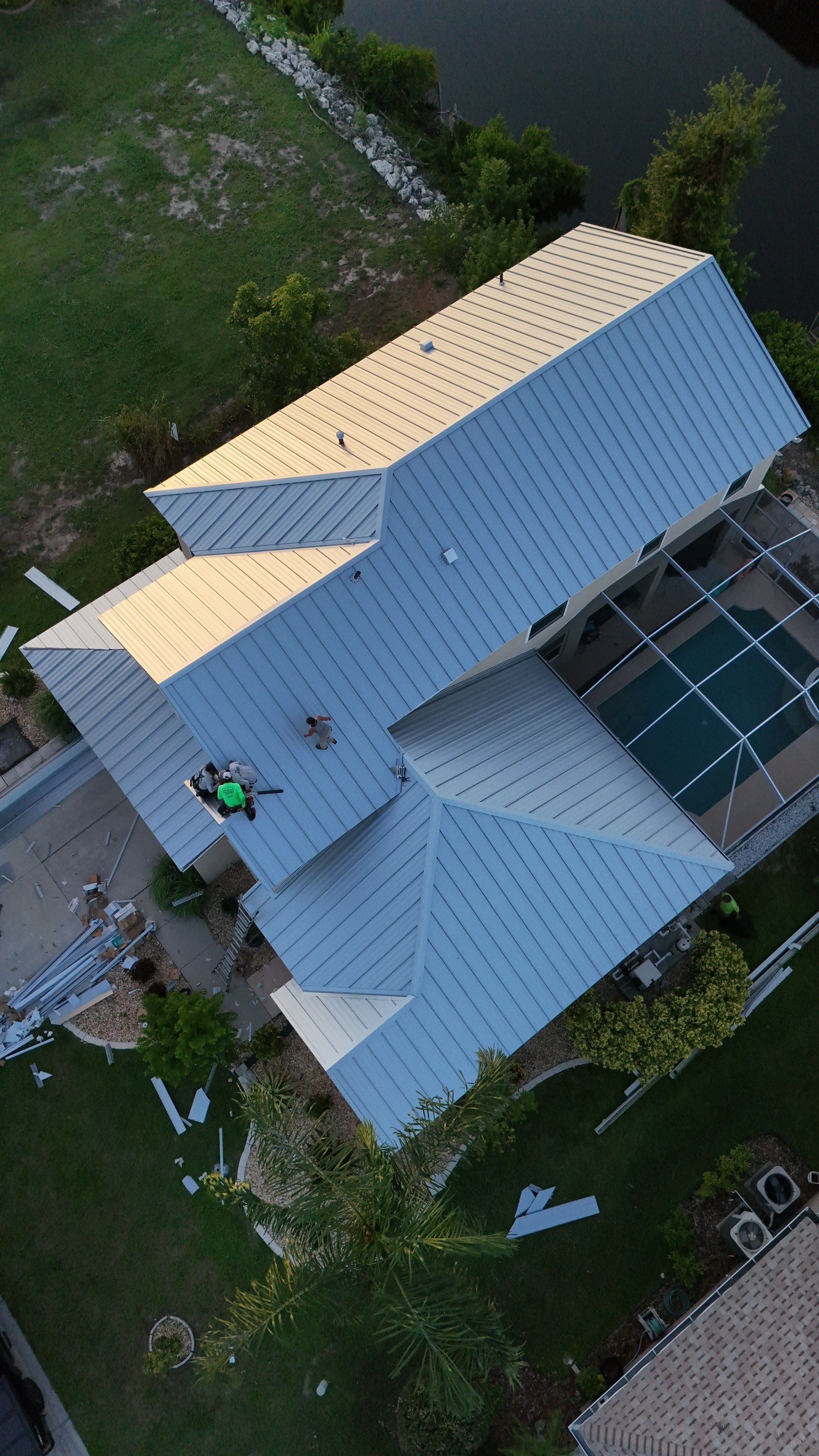 Aerial view of a light blue house with multiple roof sections and a backyard pool.